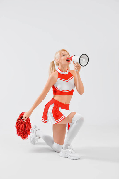 Beautiful cheerleader with megaphone on light background - Foto, afbeelding