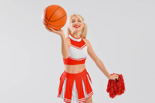 Beautiful cheerleader with ball on light background - Фото, изображение