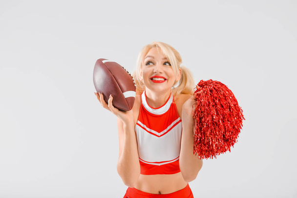 Piękna cheerleaderka z piłką rugby na jasnym tle - Zdjęcie, obraz