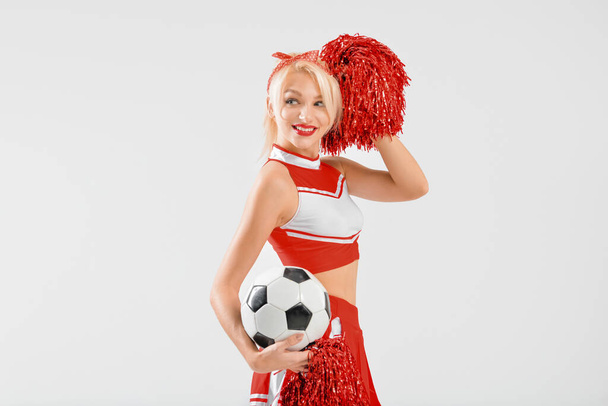 Beautiful cheerleader with soccer ball on light background - Foto, Imagem