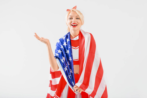Beautiful cheerleader with USA flag on light background - Foto, Imagen