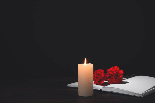 Book with carnation flowers and candle on table against dark background - 写真・画像