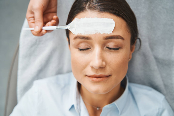 Cosmetico mano applicando un prodotto per la cura della pelle sulla fronte della donna - Foto, immagini