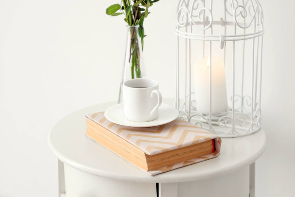 Nachttisch mit Tasse Kaffee und Buch in der Nähe der weißen Wand - Foto, Bild