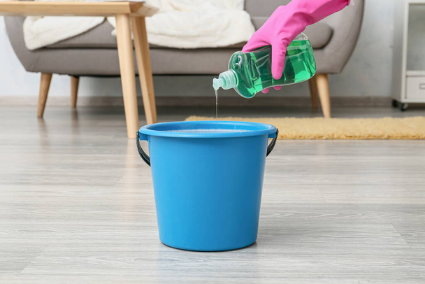 Woman pouring detergent into bucket in room - Photo, Image