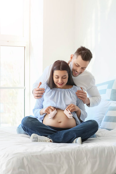 Beautiful pregnant couple with baby booties at home - Φωτογραφία, εικόνα