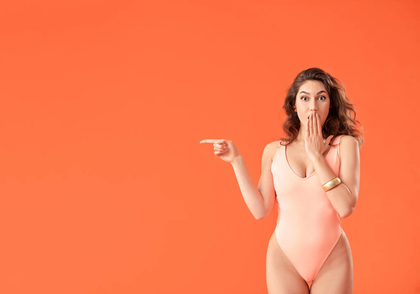 Surprised young woman in swimsuit pointing at something on color background - Photo, image