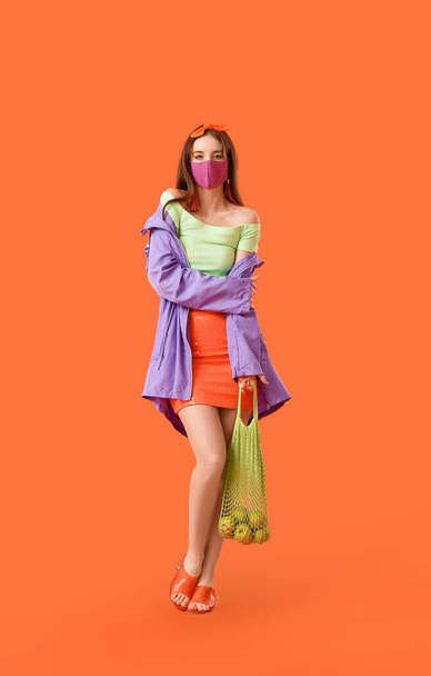 Fashionable young woman wearing mask on color background - Foto, afbeelding
