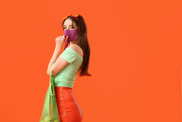 Модная молодая женщина в маске на цветном фоне - Фото, изображение