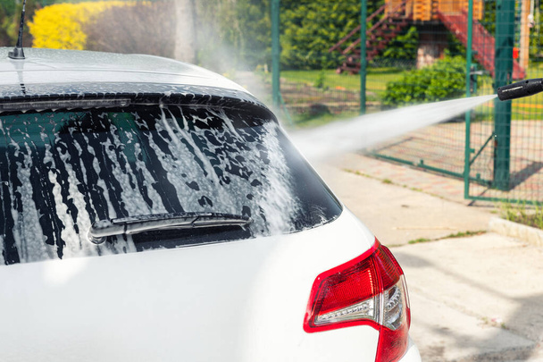 Détail détaillé lavage manuel de voiture avec pompe à eau à haute pression et éponge savonneuse à la maison arrière-cour journée d'été en plein air. Véhicule recouvert de mousse shampooing détergents chimiques lave-auto libre-service - Photo, image