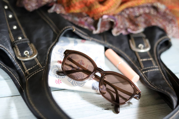 Obsah černé kožené tašky na rameno (sluneční brýle, balzám na rty a skládací zrcadlo) a pleteného snoodu, módní zboží - Fotografie, Obrázek