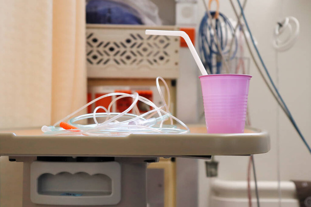 Tubes and a plastic drinking cup with a straw on a table in a hospital room. - Photo, Image
