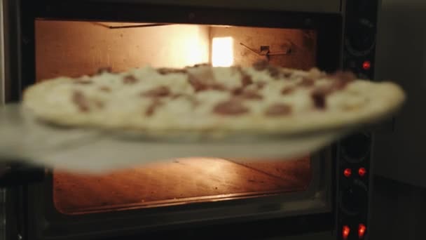 Szef kuchni kładzie wypełnioną pizzę na naczyniu do pieczenia w piekarniku na drewnianej kulinarnej łopatce. Zbliżenie - Materiał filmowy, wideo