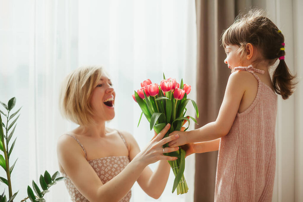 Happy mother's day! Little girl congratulating her mother and giving her flowers. Mom and daughter spending time together. Focus on tulips. - Foto, immagini