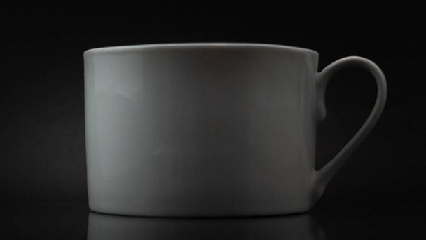A closeup shot of a white mug on a dark background - Фото, зображення
