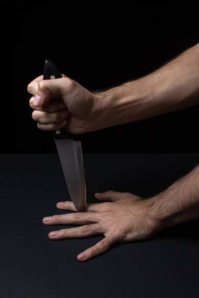 Dangerous games. knife between the fingers on a black background. Playing with a sharp knife. - Photo, Image