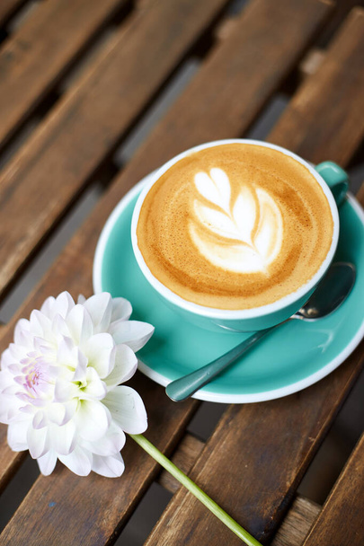 テーブルストリートカフェや庭でコーヒーカップ。花とコーヒーマグカップ。ラテアート - 写真・画像