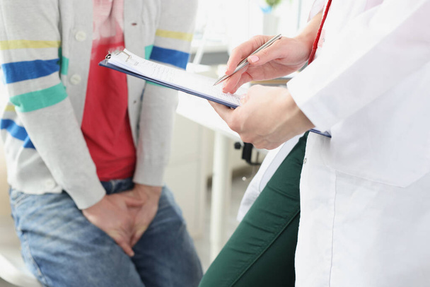 Mann sitzt beim Arzttermin und hält sich an Nahaufnahme im Genitalbereich fest - Foto, Bild