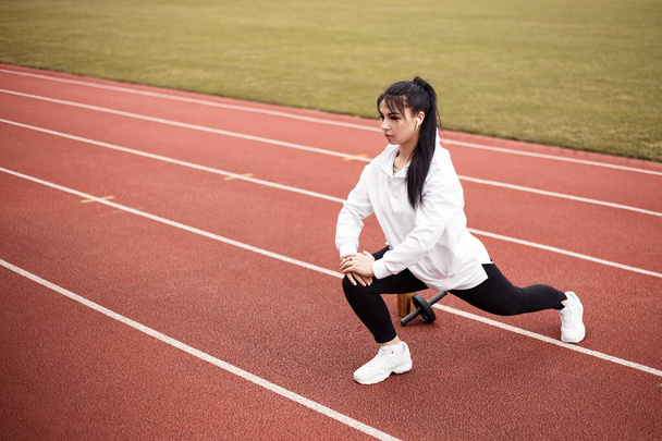 Girl stretches, prepares her body and muscles for a productive fitness workout. Flexible female dressed sports suit sporty model on the city stadium. Image with copy space. Single leg squats - Photo, image
