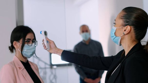 Üzleti nő arcmaszk ellenőrzése kollégák homlok hőmérséklet - Fotó, kép