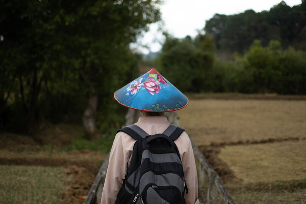 A burmese man in traditional clothing and a colorful blue hat trekking past rice fielfs from Kalaw to Inle Lake, Shan state, Myanmar - Photo, Image