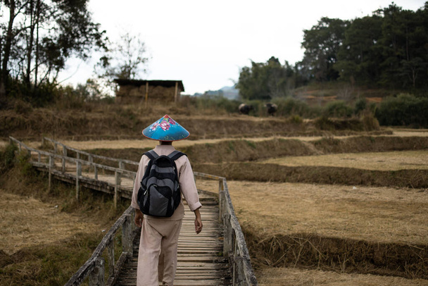 Burmese man in traditional clothing and a colorful blue hat trek a walkway past rice fields from Kalaw to Inle Lake, Shan state, Myanmar - Photo, Image