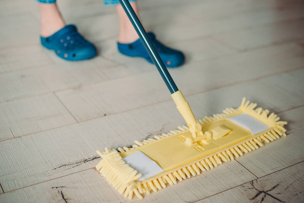 Frau putzt Fußboden zu Hause mit gelbem Wischmopp. Mikrofaser-Mopp isoliert auf weißem Holzboden Hintergrund, Nahaufnahme, drinnen - Foto, Bild