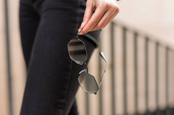 A stylish accessory. Close-up of sunglasses in a woman's hand. Outdoor portrait. - Photo, Image