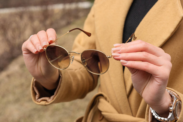 A woman in a coat holds sunglasses. Close-up outdoors. - Photo, Image