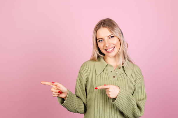Hübsche Europäerin in lässigem Strickpullover auf rosa Hintergrund glücklich erstaunt aufgeregt Punkt links mit Zeigefinger - Foto, Bild