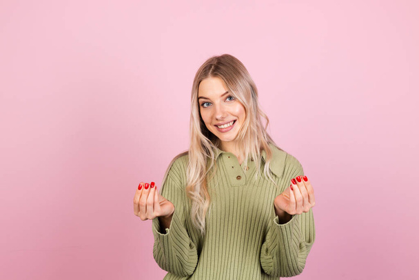 Pretty european woman in casual sweater on pink background rubbing fingers doing money gesture - Photo, Image