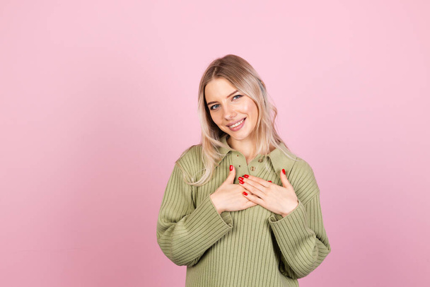 Mujer bastante europea en suéter casual sobre fondo rosa sosteniendo las manos dobladas en el pecho, espacio para copiar el corazón - Foto, imagen