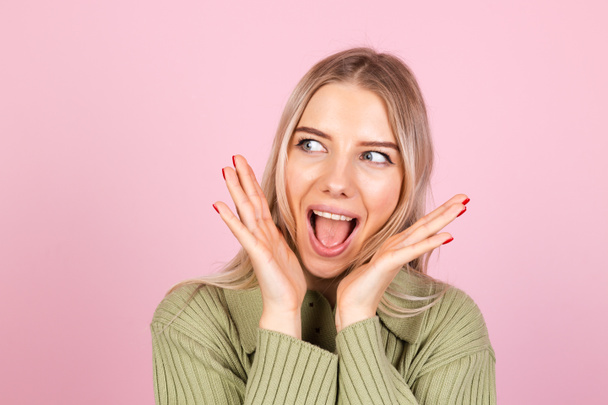 Pretty european woman in casual sweater on pink background happy look to camera shocked amazed surprised open mouth - Photo, Image