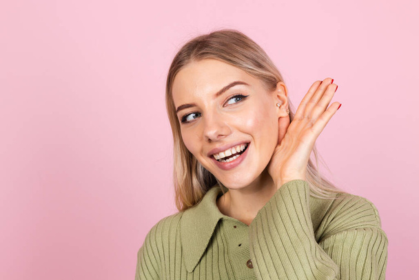 Pretty european woman in casual sweater on pink background curious try to hear what you saying with hand by ear copy space - Φωτογραφία, εικόνα