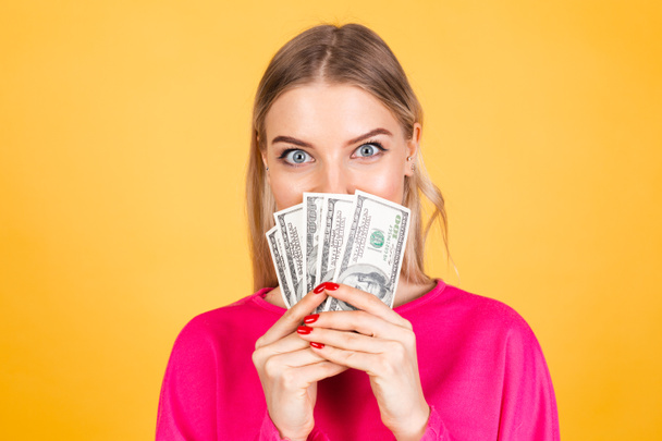Pretty european woman in pink  blouse on yellow background hold fan of 100 dollars money and, excited surprised cover face - Foto, imagen