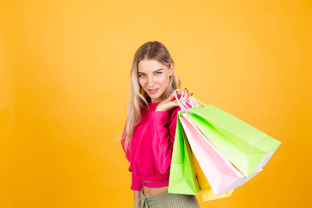 Hübsche Europäerin in pinkfarbener Bluse auf gelbem Hintergrund mit Einkaufstaschen schockiert aufgeregt isoliert Kopierraum - Foto, Bild