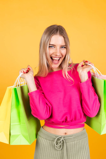 Melko eurooppalainen nainen vaaleanpunainen pusero keltaisella taustalla tilalla ostoskassit yllättynyt järkyttynyt tunteita, alennus myynti edistäminen käsite iloinen onnellinen - Valokuva, kuva