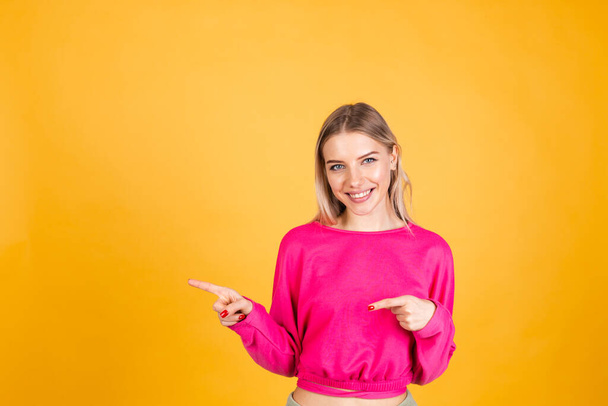 Mooi europees vrouw in roze blouse op gele achtergrond blij enthousiast vrolijk punt links met index vinger - Foto, afbeelding