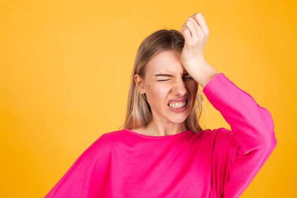 Pretty european woman in pink  blouse on yellow background preoccupied put hand on head look aside copy space - Fotografie, Obrázek