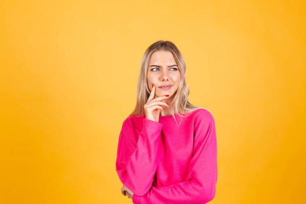 Pretty european woman in pink  blouse on yellow background looks to the side thoughtfully with a sweet smile - Фото, зображення