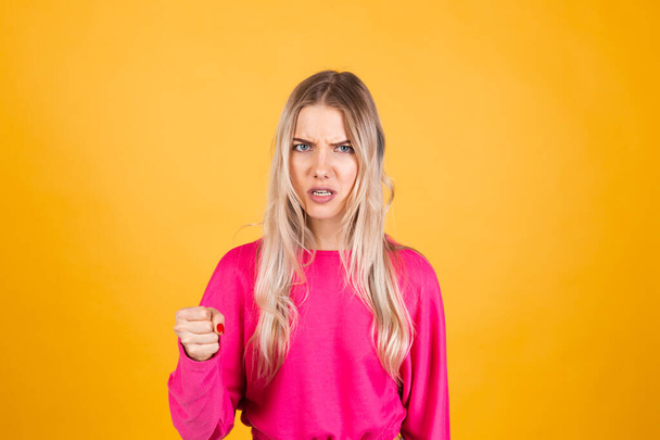 Pretty european woman in pink blouse on yellow background shouts angrily, reproachfully accuses you, points directly to camera, blames you - Foto, immagini