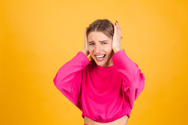 Pretty european woman in pink blouse on yellow background covering ears with hands with annoyed expression for the noise of loud music - Photo, Image