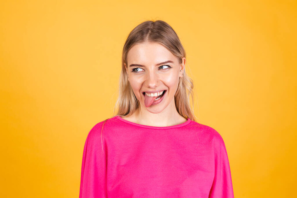Красивая европейская женщина в розовой блузке на желтом фоне торчащий язык счастлив с смешным выражением делает смешные гримасы - Фото, изображение