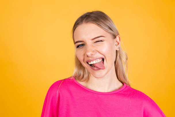 Mujer bastante europea en blusa rosa sobre fondo amarillo sacando la lengua feliz con expresión divertida hace muecas divertidas - Foto, Imagen