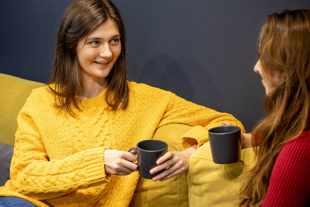 young lesbian couple talking on couch with cup of coffee - Photo, Image