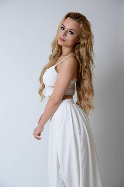 Polnisches Model posiert mit weißem Oberteil, langem weißen Kleid mit Schnitt und zeigt ihre Beine. - Foto, Bild
