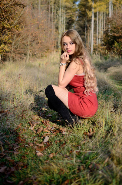 Тепла осінь у Польщі. Молода жінка з червоним платтям оточена деревами. Жінка з білявим волоссям. - Фото, зображення
