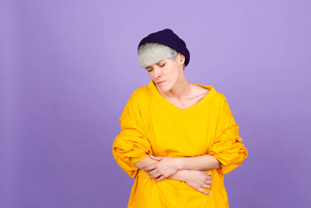 Стильная европейская женщина на фиолетовом фоне, страдающая болью в животе с болезненной гримасой, ощущающая внезапное сумасшествие периода, гинекологическое понятие - Фото, изображение