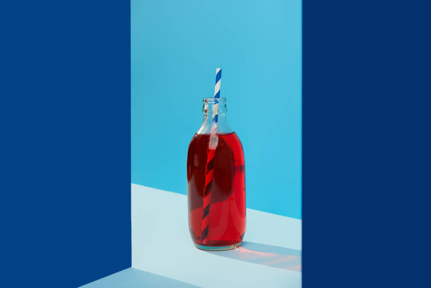 Refreshing cranberrie lemonade cocktail in bottle with palm leaf on blue creative background - Foto, afbeelding