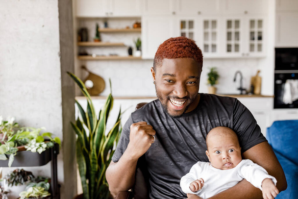 african american father and his adorable baby boy sitting on sofa at home - Фото, изображение